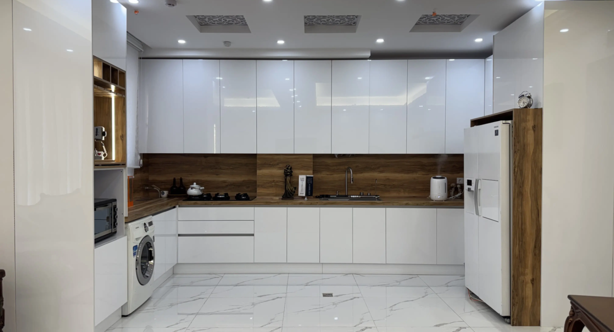 نمونه اجرای کابینت هایگلاس سفید براق با ترکیب مات و براق، صفحه و بینکابینتی طرح چوب، طراحی مدرن آشپزخانه توسط کابینت صحرایی با نورپردازی سقفی و چیدمان کلاسیک میز ناهارخوری